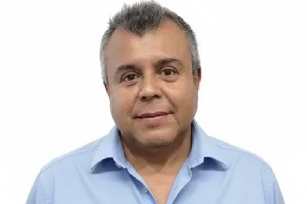 Man with graying hair in a gray shirt, smiling against a white background.